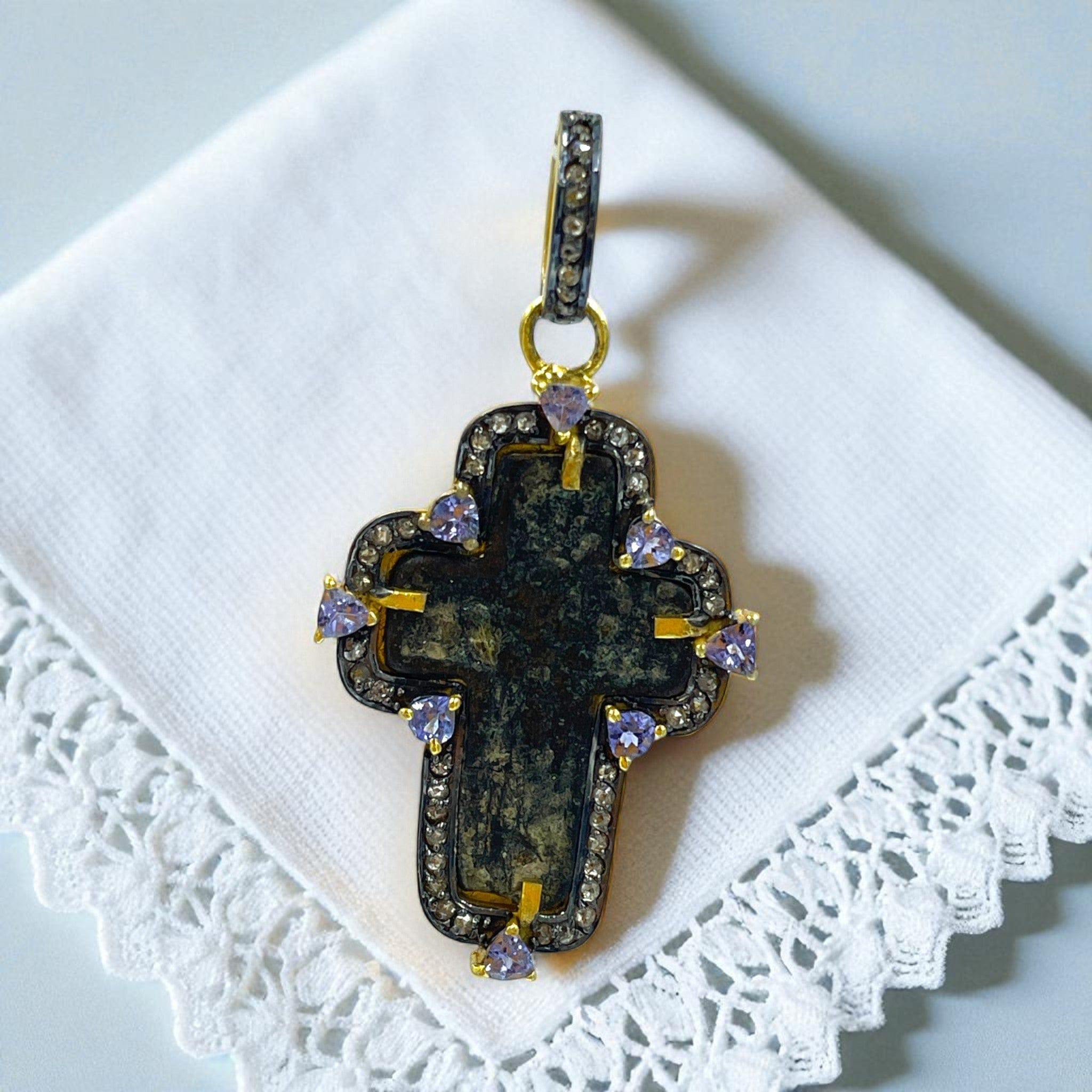 Close-up of authentic 17th–18th century sand-cast copper Old Believers Christian cross with historical patina and engravings, set in 24kt gold-plated sterling silver with diamond and tanzanite accents on a lace napkin. 
